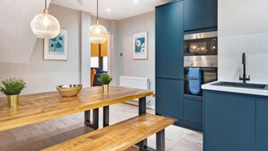 A modern kitchen with a wooden table, bench, pendant lights, and a built-in oven. - Host Apartments The Coachouse at Pilgrim St (Liverpool)