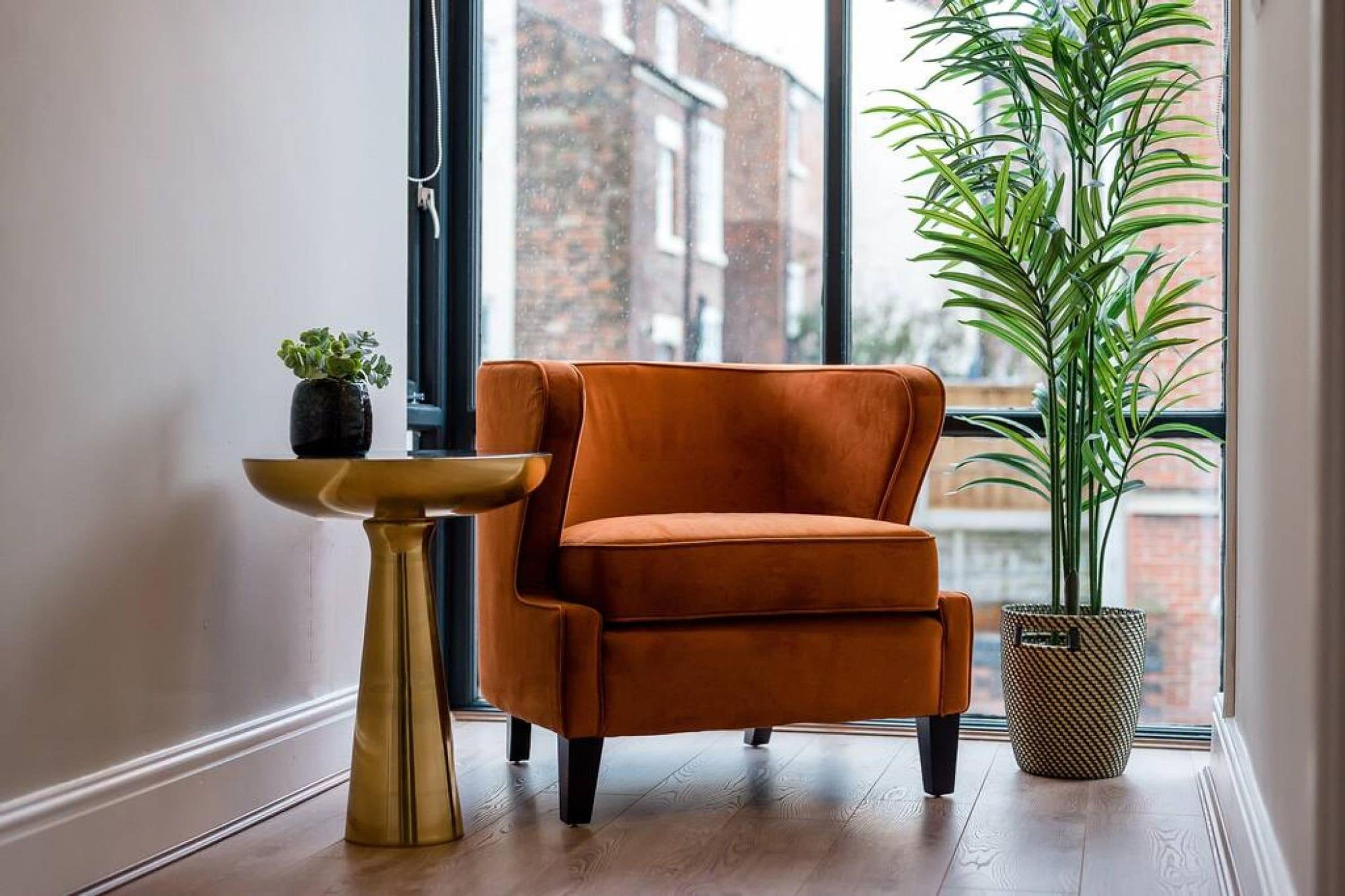 A room with a large window, a potted plant, a small table, and an orange chair.