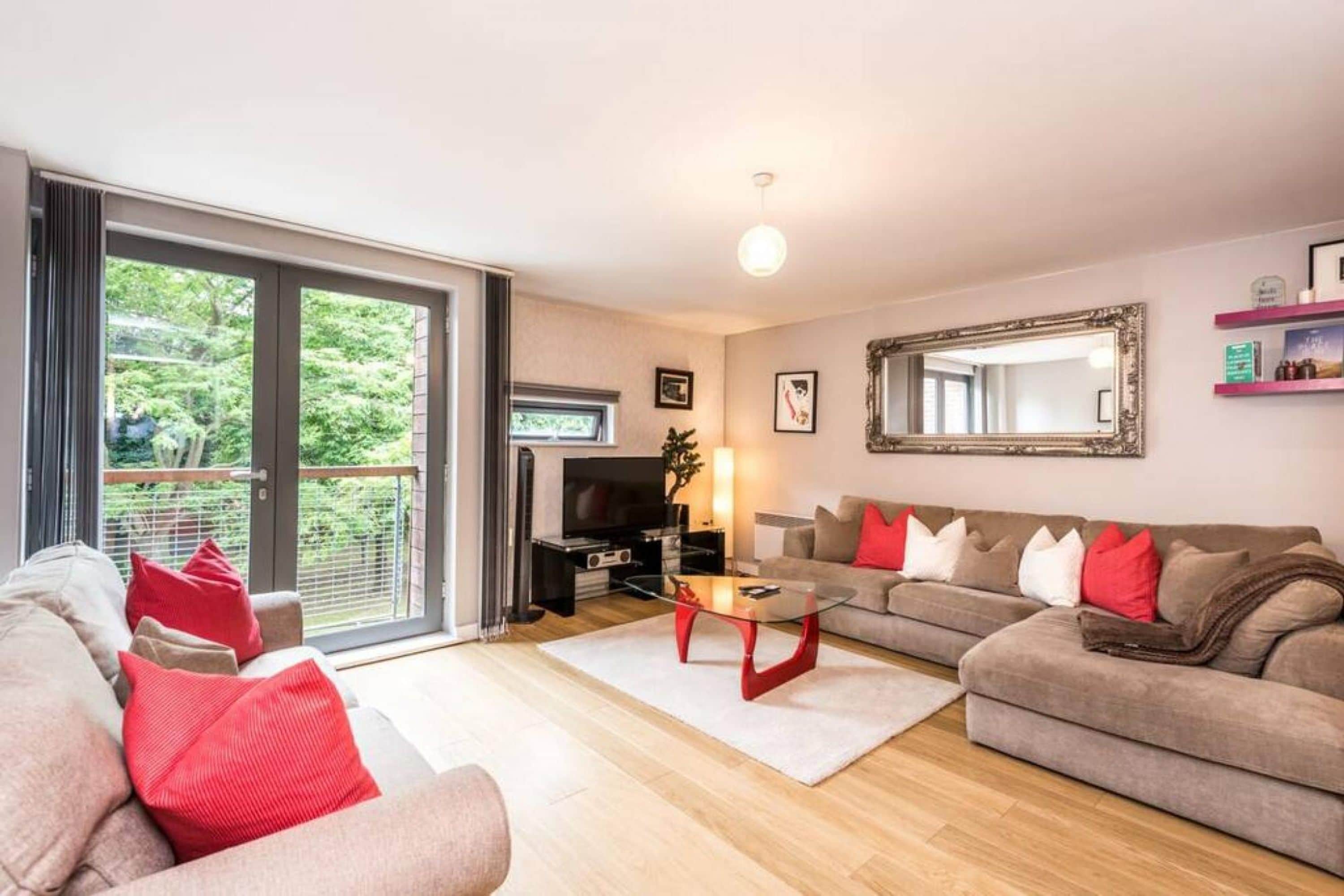 A living room with a sofa, a coffee table, and a television. There is a sliding glass door leading to a balcony.