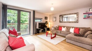 A living room with a sofa, a coffee table, and a television. There is a sliding glass door leading to a balcony. - Host Apartments York Place Apt (Liverpool)