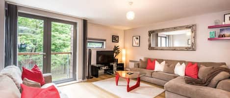 Een woonkamer met een bank, een salontafel en een televisie. Er is een schuifpui die leidt naar een balkon.