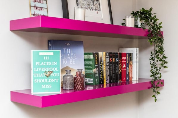 Uno scaffale rosa con libri, una cornice e bottiglie decorative.