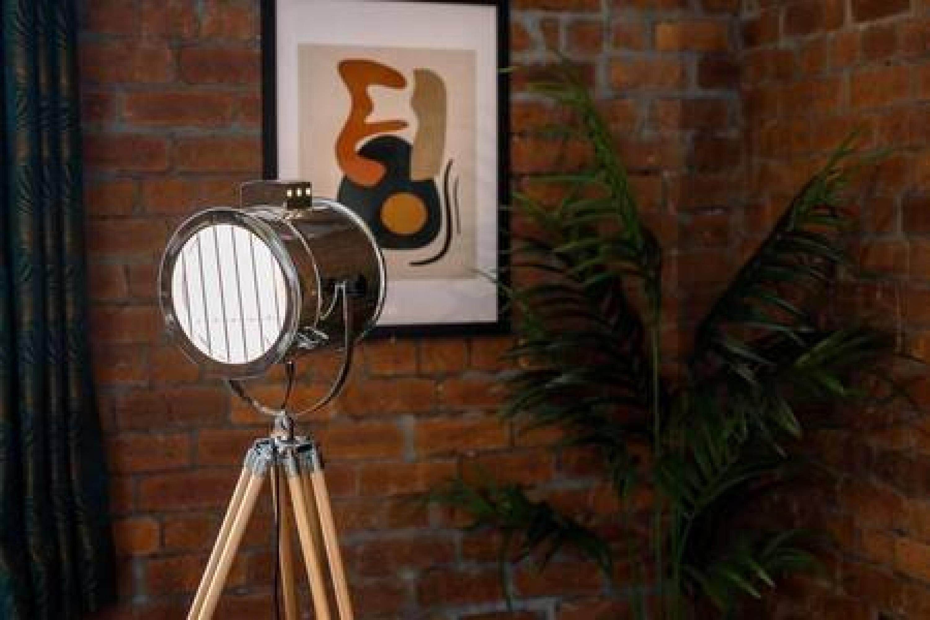 A vintage camera on a tripod against a brick wall with a framed abstract painting.