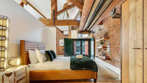 Quarto com cama de madeira, parede de tijolos e teto de madeira.