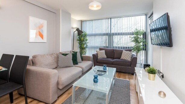 A modern living room with two sofas, a coffee table, and a TV mounted on the wall. - Host Apartments Standish Street Living (Liverpool)