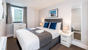 A modern hotel room with a large bed, two bedside tables, a window with curtains, a framed picture on the wall, and a mirror on the wall. - Host Apartments Standish Street Living (Liverpool)
