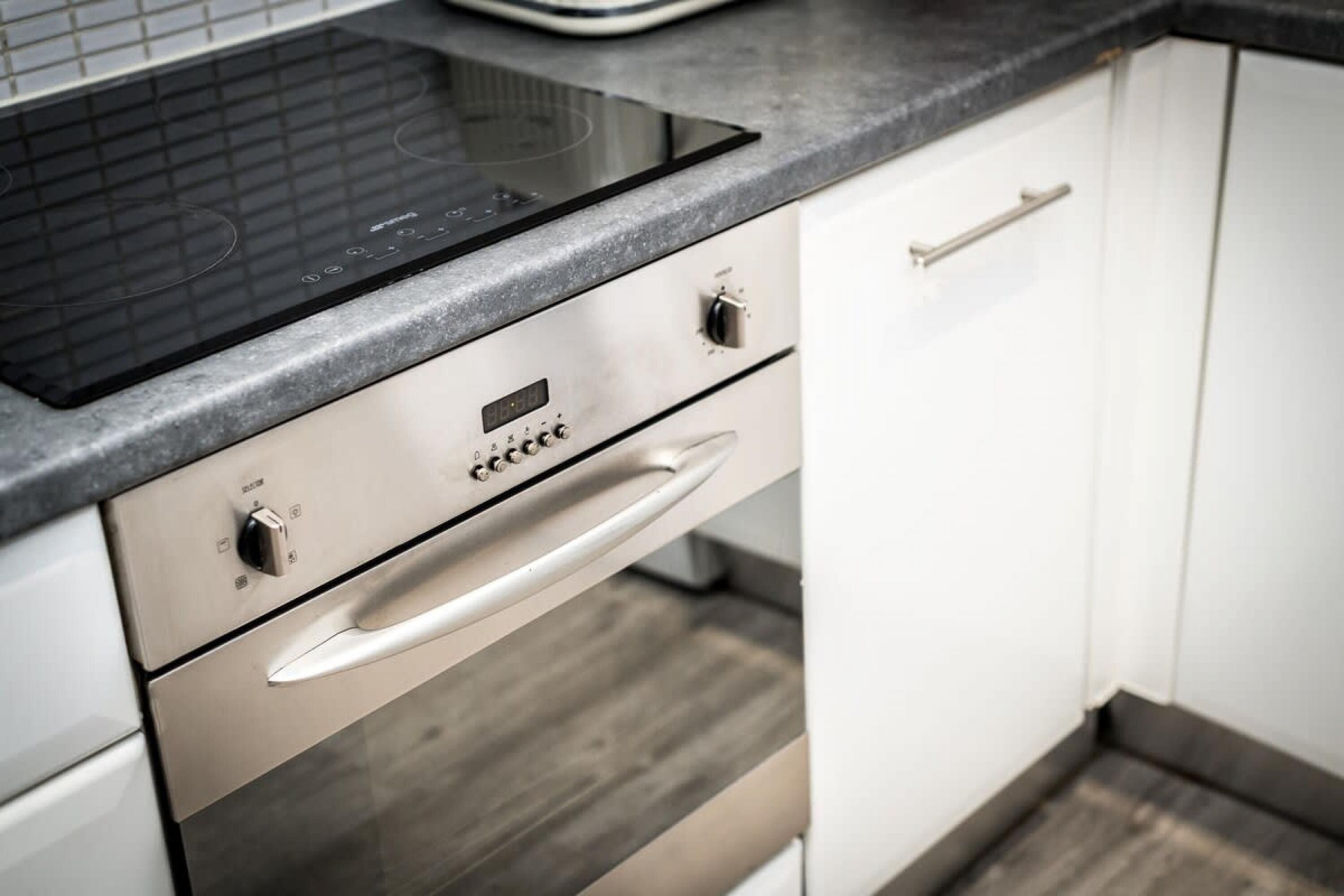 A kitchen with a built-in induction cooktop, a stainless steel oven, and a white cabinet with a handle.