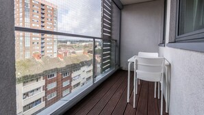 Uma varanda com vista para a paisagem urbana, uma cadeira branca e uma mesa pequena.