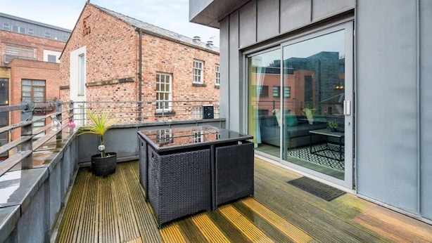 Une terrasse sur le toit avec une porte vitrée donnant sur un patio, un bâtiment en briques en arrière-plan et une plante en pot sur la terrasse en bois.