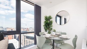 A modern dining area with a round table, green chairs, and a potted plant. - Host Apartments The Baltic Penthouse 3 (Liverpool)