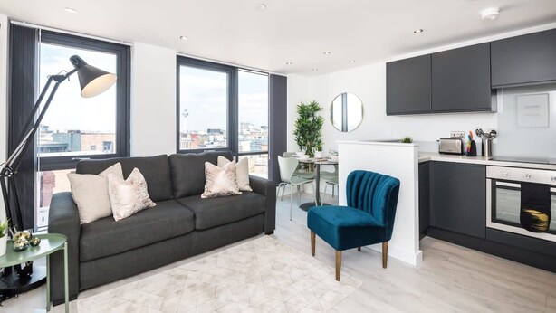 A modern apartment with a grey sofa, a blue chair, a dining area, and a kitchen. - Host Apartments The Baltic Penthouse 3 (Liverpool)