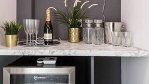 A bar area with a neon sign reading "Shall We?", a bottle of champagne, glasses, and decorative plants. - Host Apartments Seel St Townhouse Apt I (Liverpool)