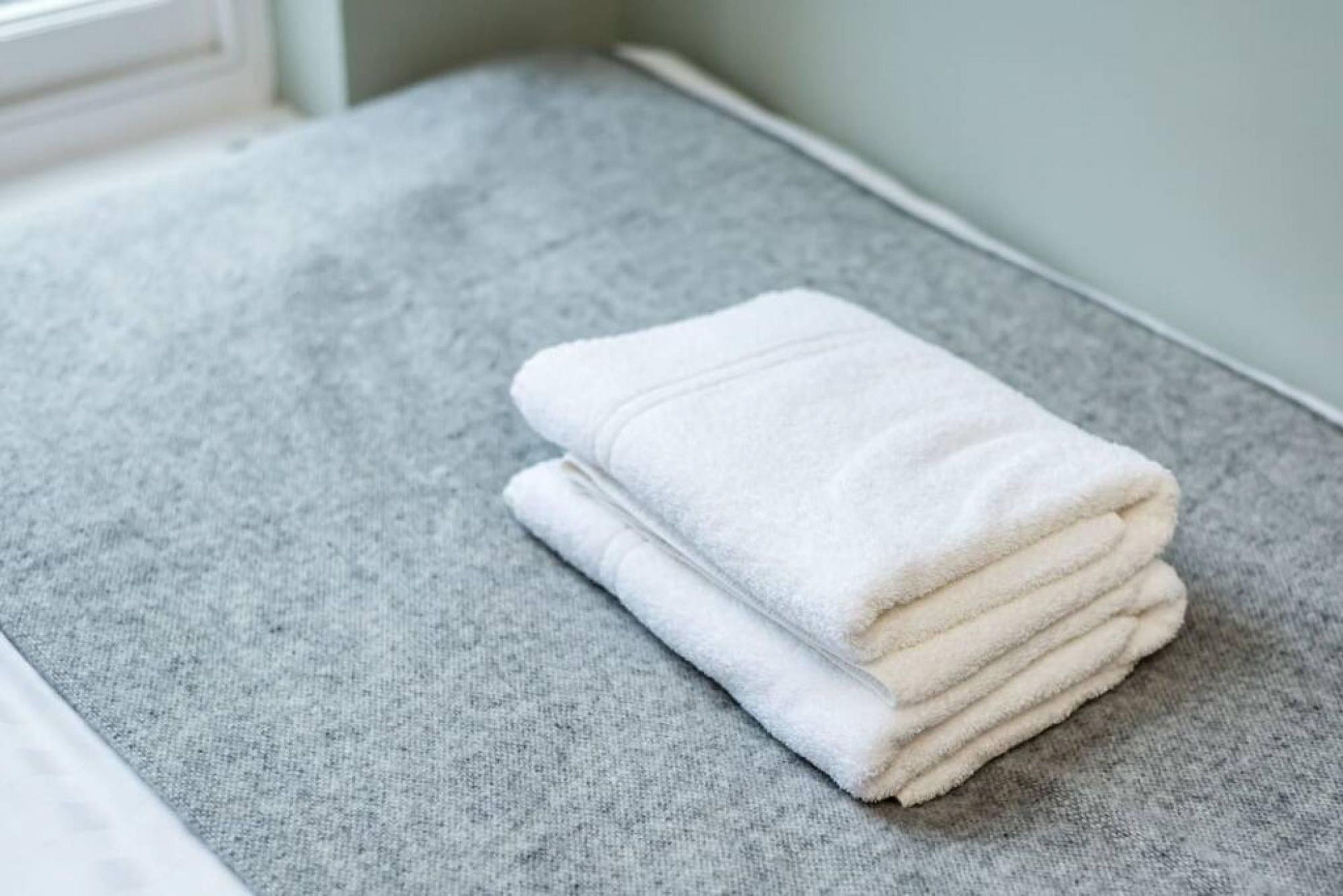 A neatly folded white towel on a grey carpeted floor.