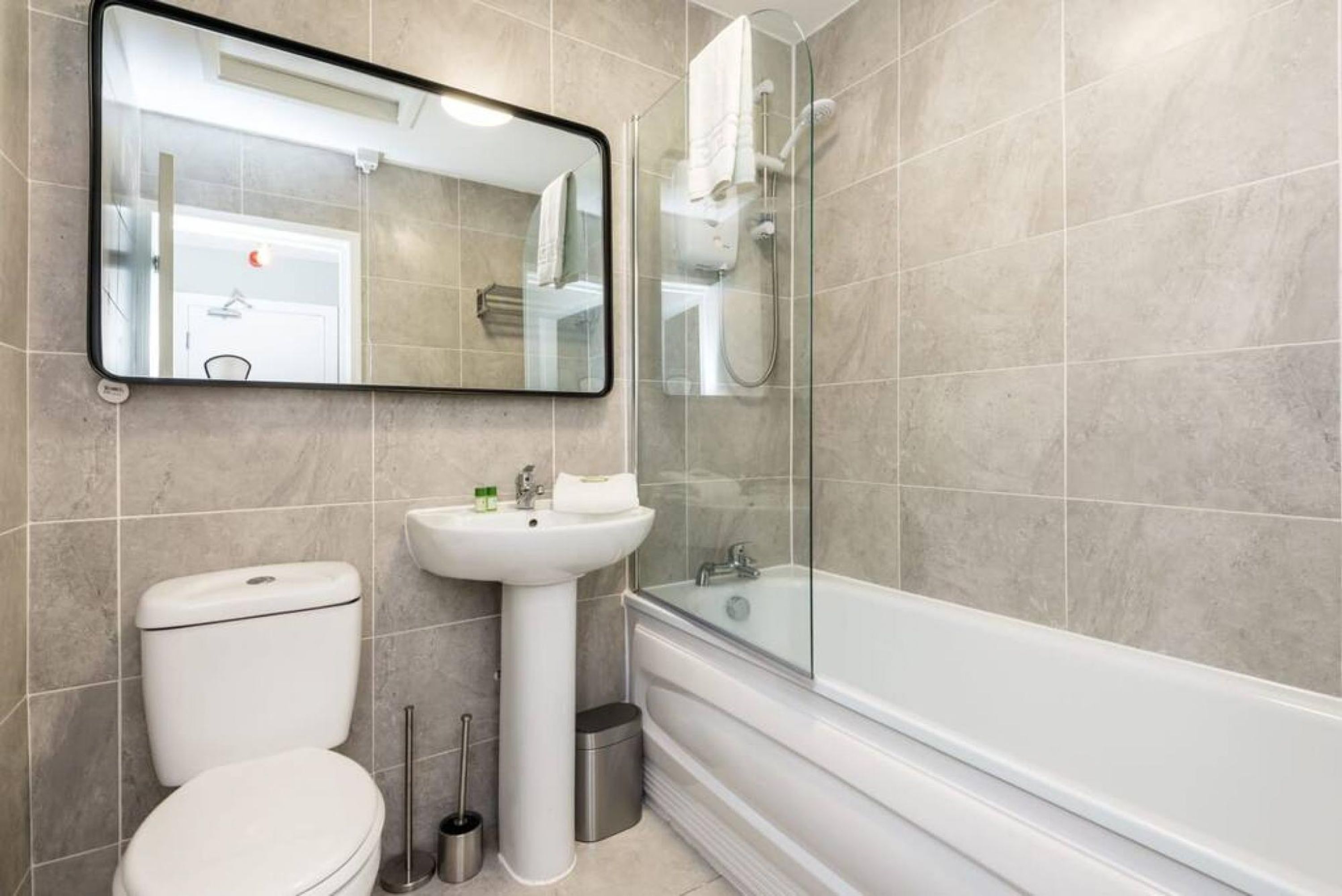 Une salle de bain moderne équipée de toilettes, d’un lavabo sur colonne et d’une baignoire entourée de parois en verre.
