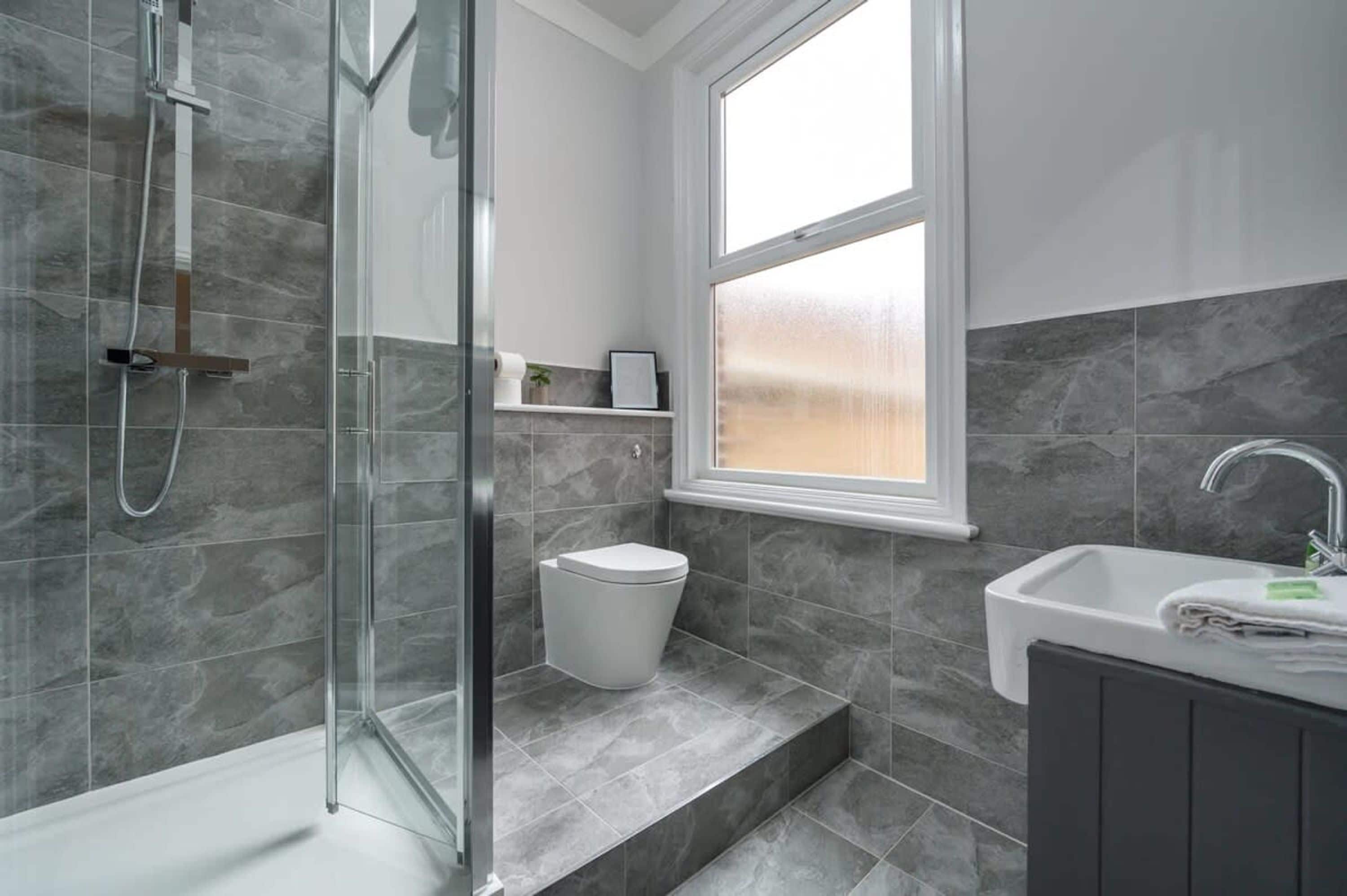 Un baño moderno con cabina de ducha de vidrio, inodoro y lavamanos con espejo.