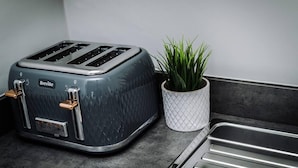 A Breville toaster with a textured surface, a power cord, and a white plant in a textured pot on a kitchen counter. - Host Apartments The Bank Apt (Liverpool)
