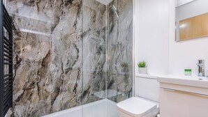 A bathroom with a marble shower wall, a glass-enclosed bathtub, a white toilet, and a white sink with a mirror above it. - Host Apartments The Bank Apt (Liverpool)