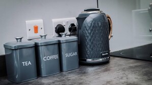 A kitchen counter with three gray containers labeled "TEA," "COFFEE," and "SUGAR," and a Breville coffee maker. - Host Apartments The Bank Apt (Liverpool)