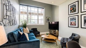 A modern living room with a blue sofa, a coffee table, and a TV. There are framed pictures on the wall and a large window with a view of the outside. - Host Stay Catharine Quarters I (Liverpool)