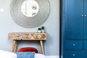 A room with a round mirror, a wooden console table with decorative elements, a blue wardrobe, and a red cushion. - Host Stay Catharine Quarters I II (Liverpool)