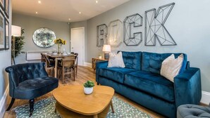 A living room with a blue sofa, a dark armchair, a wooden coffee table, and a dining area with a table and chairs.