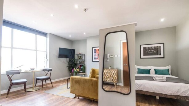 Een moderne hotelkamer met een bed, een bureau en een stoel. Er is een grote spiegel, een televisie en een lijst aan de muur.