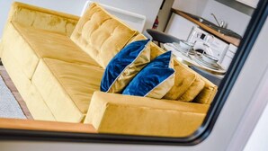 A yellow sofa with blue cushions in a room with a kitchen area visible through an open door. - Host Apartments The Georgian Quarters at Bedford (Liverpool)