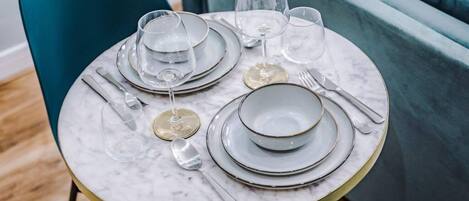 A table set with plates, glasses, and cutlery, with a teal chair and a marble table.