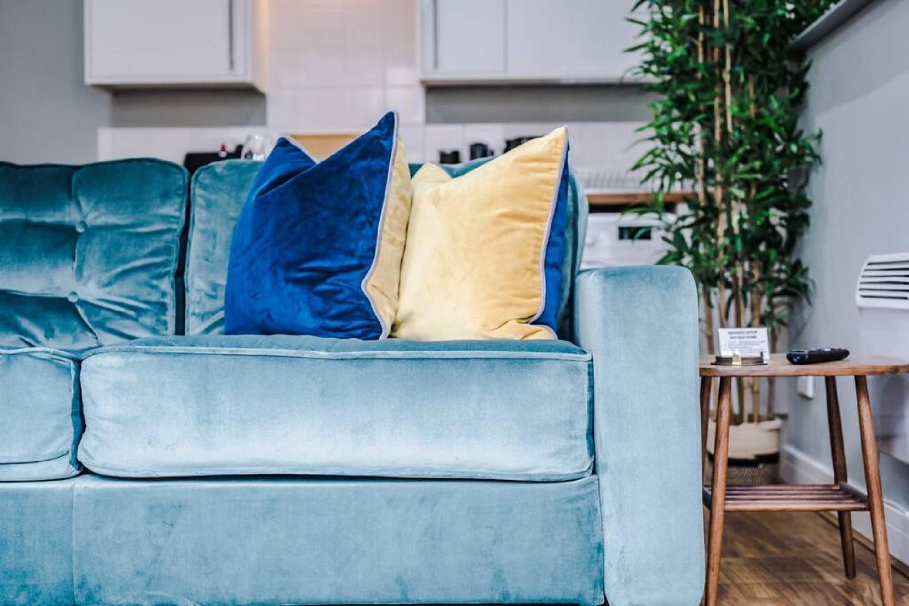 A teal sofa with blue and yellow cushions in a modern kitchen setting.