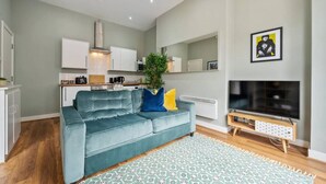 A modern living room with a teal sofa, a patterned rug, a TV, and a kitchen in the background. - Host Apartments The Georgian Quarters at Bedford (Liverpool)