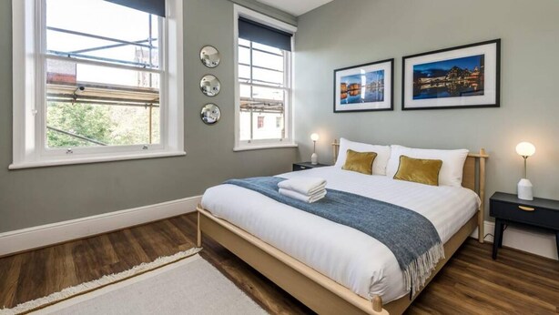 A bedroom with a bed, two windows, a nightstand, and two framed pictures on the wall. - Host Stay Catharine Quarters II (Liverpool)