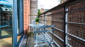 A balcony with a metal chair, a small round table, and a potted plant.