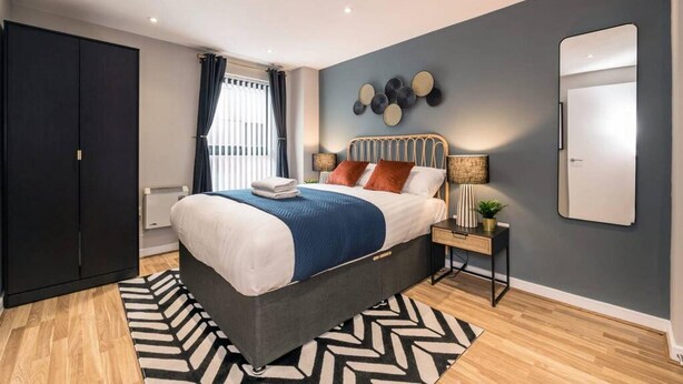 A modern bedroom with a bed, a nightstand, a mirror, and a wardrobe.