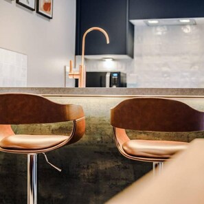 A modern kitchen with a copper faucet, two bar stools, and a microwave. - Host Apartments The Pilgrim Coach House II (Liverpool)