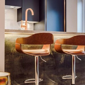 A modern kitchen with two bar stools, a stainless steel sink, and a dark backsplash. - Host Apartments The Pilgrim Coach House II (Liverpool)