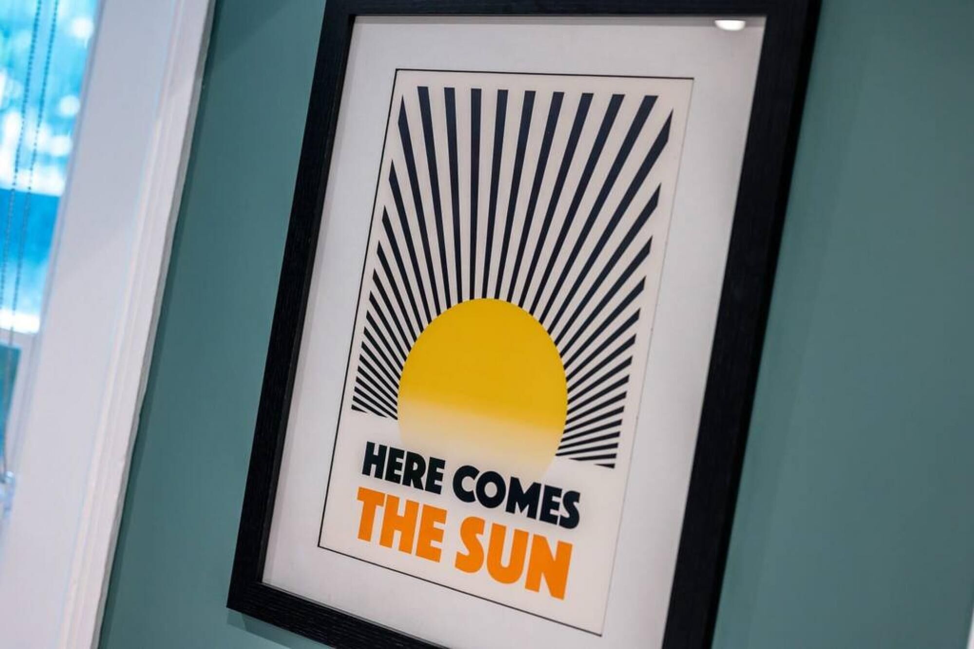 A framed poster with a sun graphic and the text "HERE COMES THE SUN".