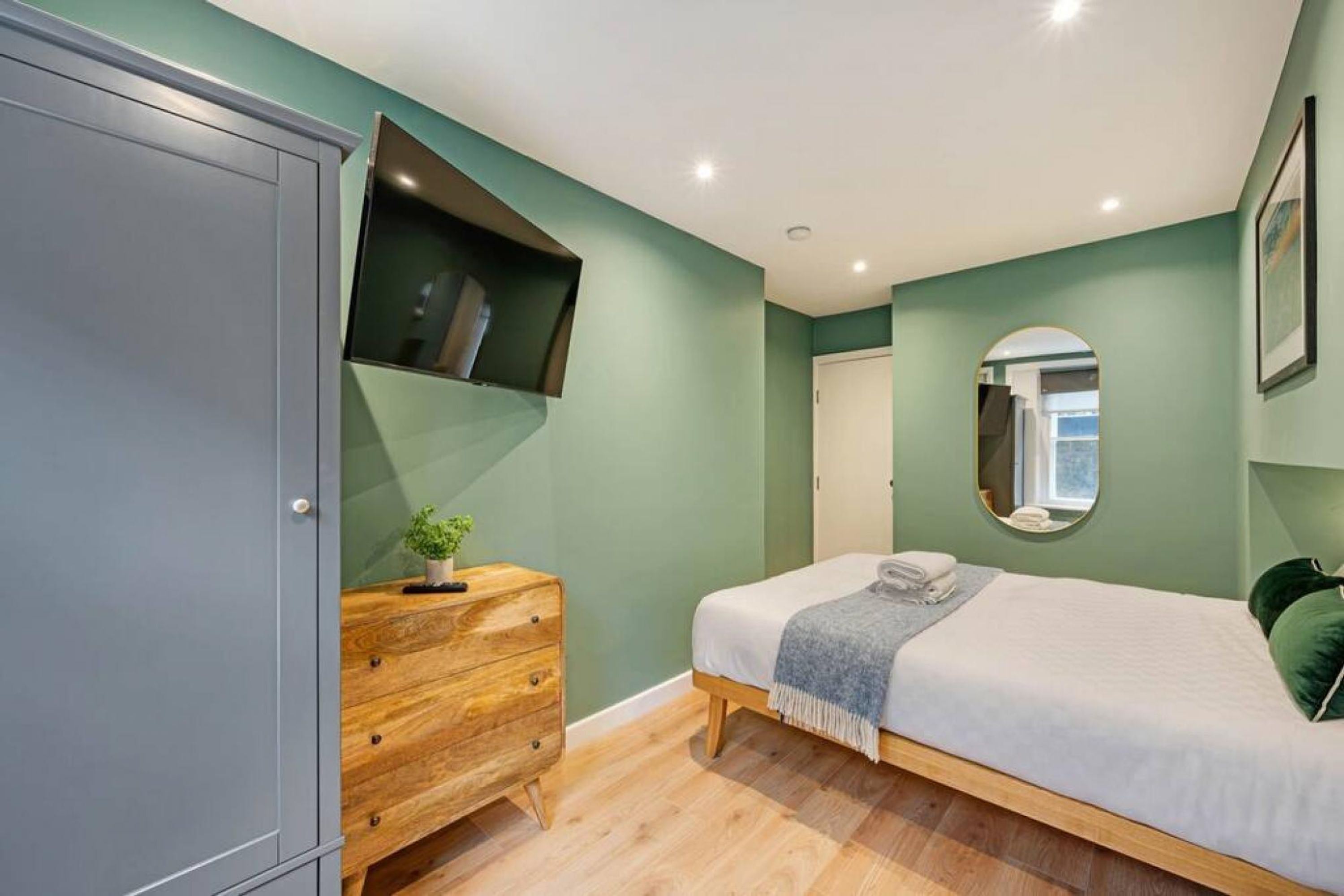 A bedroom with a bed, a dresser, a mirror, and a wardrobe.