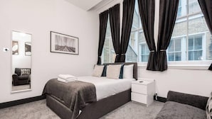 A modern bedroom with a large bed, a bedside table, a mirror, and a window with curtains.