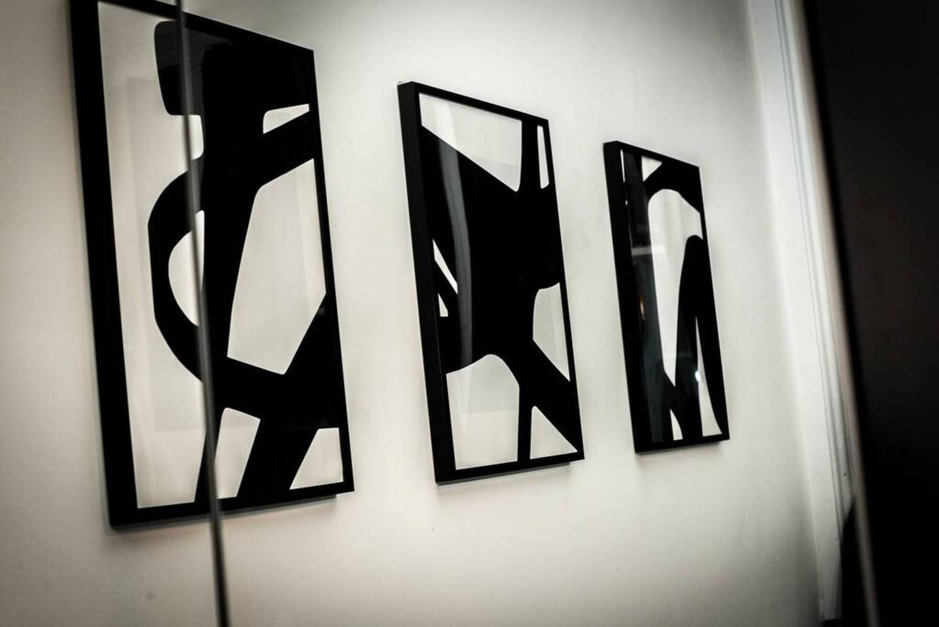 Trois œuvres d’art abstraites en noir et blanc sur un mur blanc.