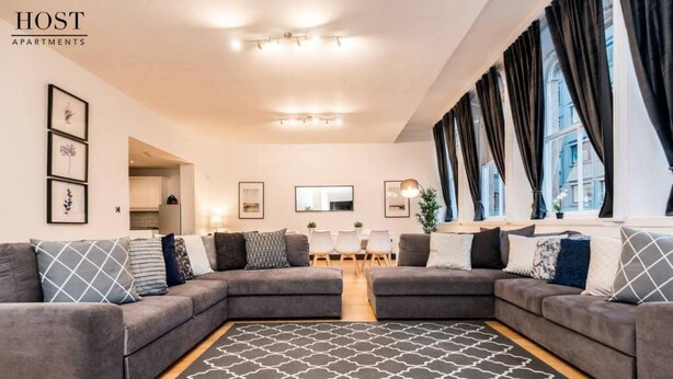 A modern living room with a sectional sofa, a patterned rug, and large windows with curtains.