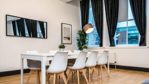 A modern dining area with a white table and chairs, a floor lamp, a framed picture, and a window with curtains.