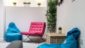 Une pièce moderne avec un fauteuil rouge, deux poufs bleus, une petite table et une grande plante verte.