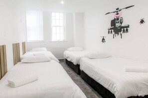 A hotel room with three single beds, a large window with sheer curtains, and a wall decal of a helicopter.