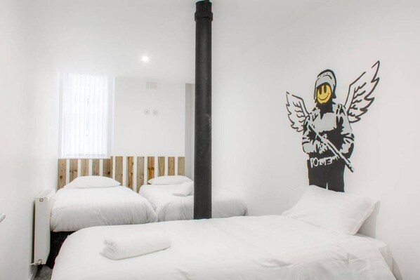 A bedroom with two beds, a wooden headboard, a black pipe, and a wall mural of a figure with wings.