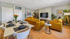 A modern living room with a dining area, featuring a sofa set, a TV, and a small table with a lamp. - Host Apartments Upper Duke Street Apartment (Liverpool)