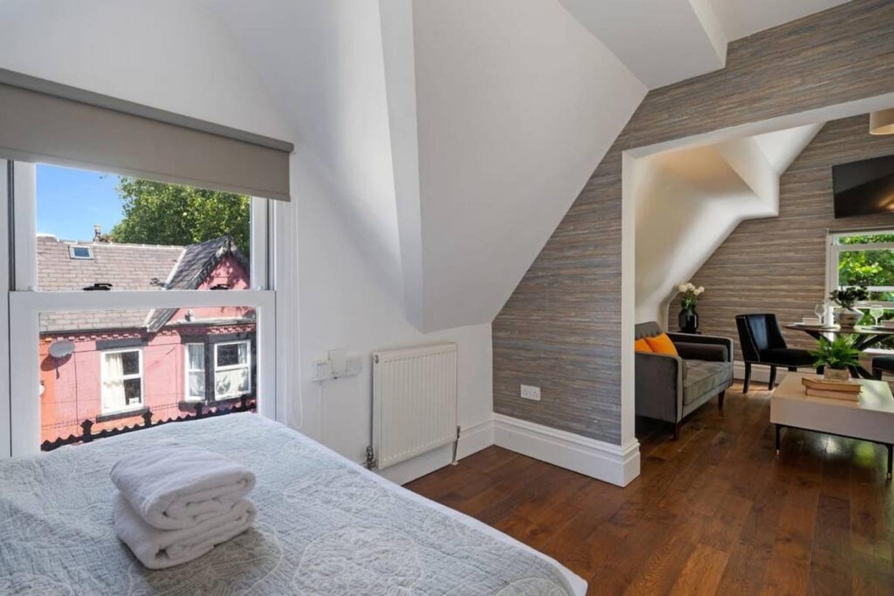 Una camera da letto moderna con un'ampia finestra, un letto rifatto con cura e vista sui palazzi vicini.