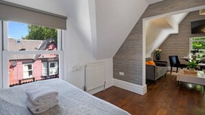 Une chambre moderne avec une grande fenêtre, un lit soigneusement fait et une vue sur les bâtiments voisins.