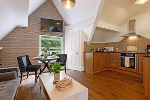 A modern kitchen with wooden cabinets, a dining area with a table and chairs, and a view of greenery outside. - Host Apartments Kensington Quarters III (Liverpool)