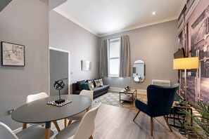 A modern living room with a grey sofa, a round dining table, and a blue armchair. - Host Apartments Halifax House II (Liverpool)