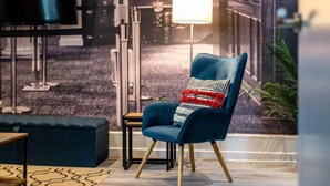 A modern living room with a blue armchair, a small side table, a floor lamp, and a television mounted on the wall. - Host Apartments Halifax House II (Liverpool)